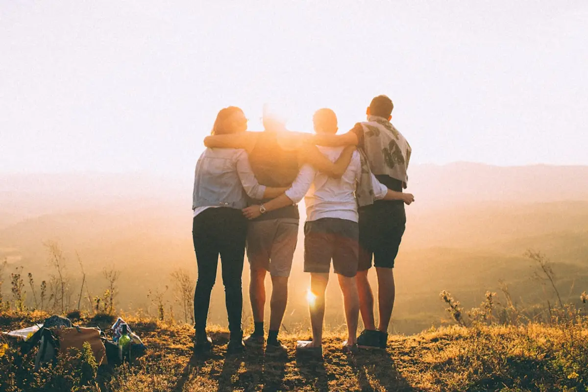 four people standing together at sunset, arms around each other, facing the horizon