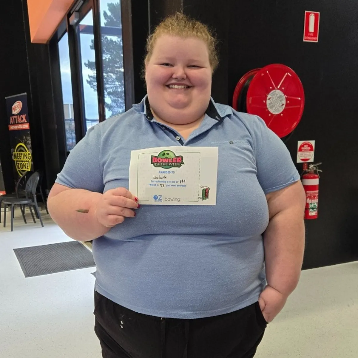 person holding a certificate with a smile, wearing a blue shirt