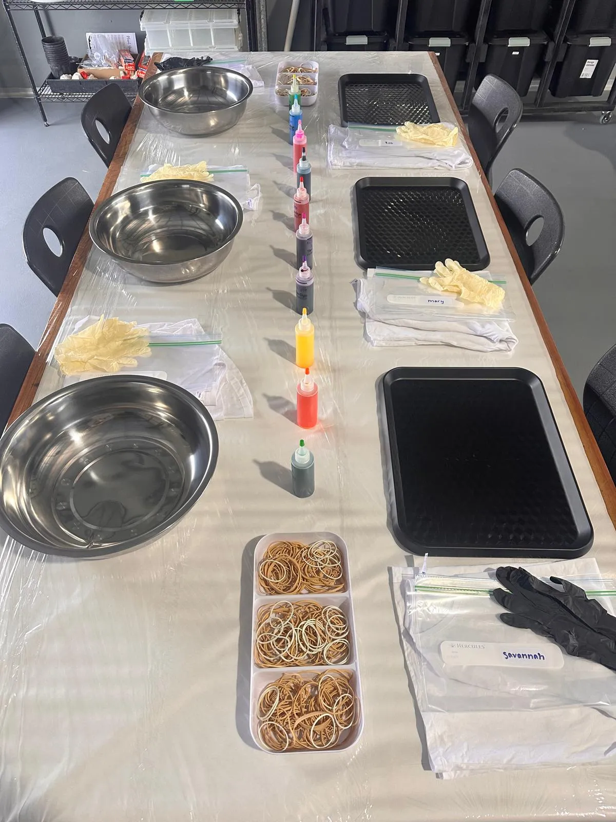 tie-dye workshop setup with bowls, dye bottles, rubber bands, and gloves on a table