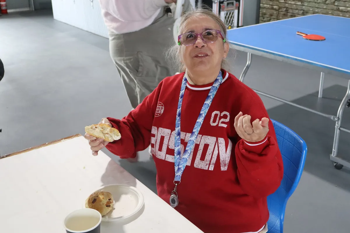 person in red boston sweatshirt eating a scone at a table with a blue lanyard and a cup of coffee